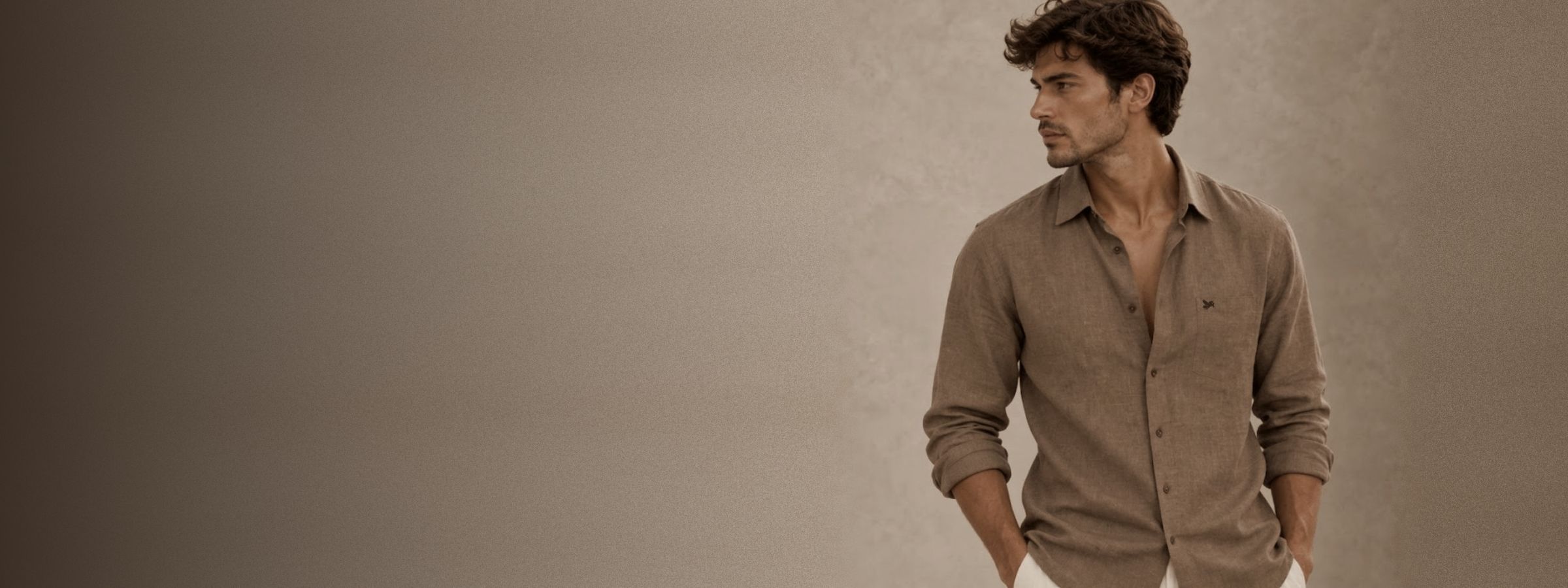 A man in a smoked-taupe French linen shirt with a small unicorn embroidery, against warm stone